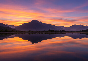 Fototapeta premium Beautiful sunset over mountains and water in the middle of a lake.