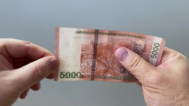 Horizontal 4K video close up. Man checking watermark with portrait of writer William Saroyan and pomegranate on 5000 dram. Cash money of Armenia. Salary, bribe, tax, loan, debt, pay. Bank. Male hand