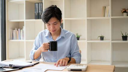 Businessman drinking coffee while working on budget planning at modern office.
