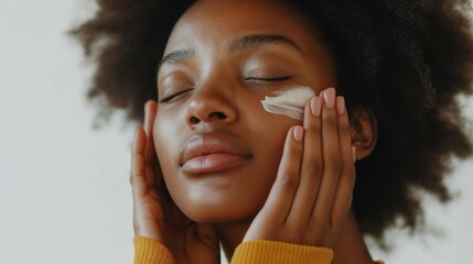 Close-up of young Black woman massaging sunscreen into face with gentle hands against clear white background