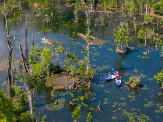 Aerial view of colorful kayaks and swimmers in a clear river at Kayak Klong Root Viewpoint, Krabi, Thailand. Active recreation in a lush, natural setting.
