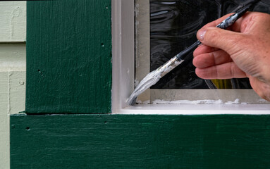 Another coat of white paint is being applied to the inside of a window sill. Masking tape has been used to protect the window.