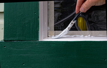 A person is painting around a window, it takes care and skill