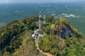 Antenna towers atop a lush, forested peak, overlooking a sprawling landscape.