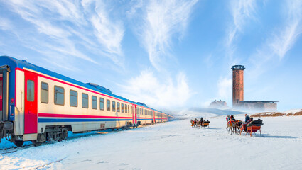 Red diesel train (East express) in motion at the snow covered railway - Horses pulling sleigh in winter - Ani Ruins, Ani is a ruined and  medieval Armenian city - Kars, Turkey