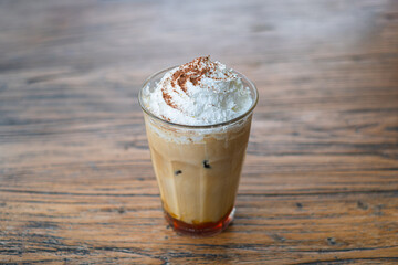 Whipped cream iced coffee with sprinkled cocoa powder on a rustic wooden table with bokeh background