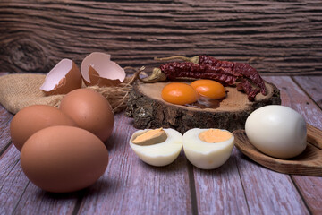Rustic food composition with fresh eggs, egg yolks, boiled eggs, and dried red chilies on a wooden...