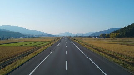 Scenic countryside road stretching to distant mountains under a clear blue sky