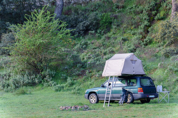 Green suv car parked in a forest camping site with rooftop tent ready for vacation trip