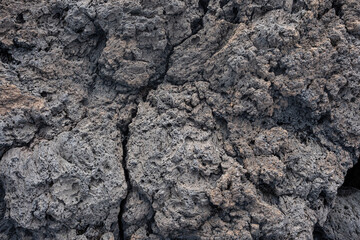 Nahaufnahme einer grau-schwarzen Lava-Textur auf dem Boden. Porös, rissig und steinern, ideal als...