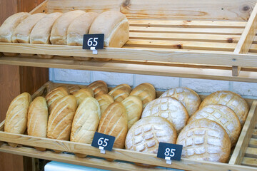 There are several loaves of wheat bread on a wooden shelf in the store.
