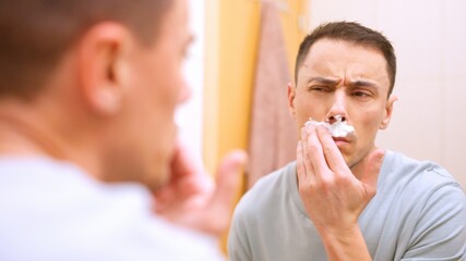 Man applying shaving cream on mustache in bathroom mirror