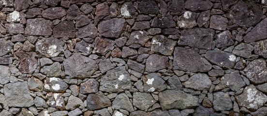 Textur Nahaufnahme einer Natursteinmauer aus Lavasteinen auf den Azoren, Portugal. Ohne Mörtel geschichtet, zeigt sie eine rustikale und natürliche Ästhetik. Eindruck von Stabilität und Tradition.