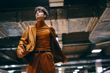 Stylish young man in a brown suit and turtleneck poses confidently in an urban underground location