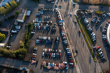 Aerial drone top-down high resolution picture of a crowded car dealership parking lot in Beaverton, Oregon, with rows of parked vehicles and blooming spring trees along the lanes © Hrach
