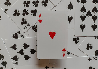Ace of Hearts playing card, positioned centrally and upright amidst a scattered collection of other playing cards. The Ace of Hearts is clearly visible with its large red heart symbol 