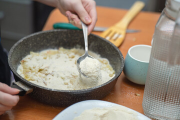metal spoon sprinkles sugar over a raw apple pie, capturing the sweet preparation of a rustic homemade dessert
