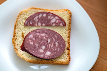 Sandwich with two slices of smoked boiled sausage featuring large white fat circles, presented on a plate for a hearty meal