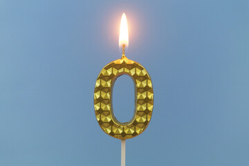 Burning gold birthday candle on blue background, number 0
