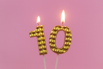 Burning golden birthday candles on pink background, number 10