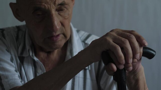Thoughtful elderly Caucasian man 75-79 years old sitting indoors with walking cane, real senior portrait, emotions of older people