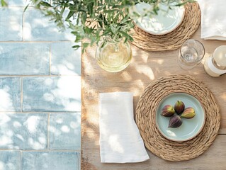 Top view of a summer dining table setting with round woven placemats, warm white linen napkins, figs, vase with green plants, against a blue tile floor in natural light, exuding summer vibes.