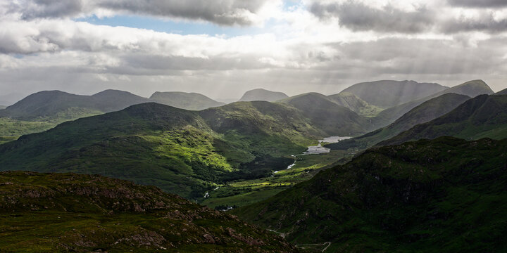 Majestic mountains surround Blackvalley in Ireland, casting shadows over the lush green landscape. The serene river winds through the valley, illuminated by soft rays of evening light.
