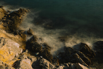 As the sun set over the ocean, waves crashed against the rock-strewn beach, painting a golden seascape and revealing a breathtaking landscape shaped by nature and sea.