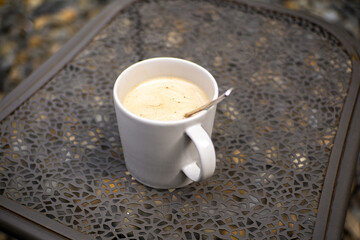 A glass of warm coffee with milk in a white ceramic cup on a gray iron table with a blurred background