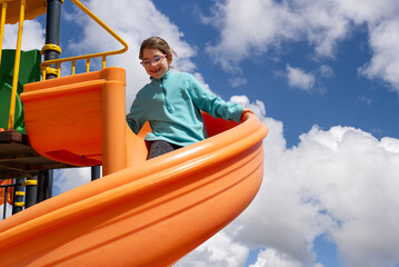 Obraz premium A cheerful little girl is playing a colorful slide in a playground in the park.