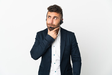 Telemarketer man working with a headset isolated on white background having doubts and thinking