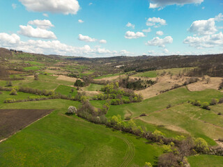 Drone footage of rural hilly landscape with trees and meadows in early spring