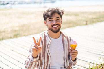 Handsome Arab man with a cornet ice cream at outdoors smiling and showing victory sign