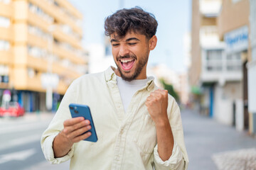 Young Arabian handsome man at outdoors with phone in victory position