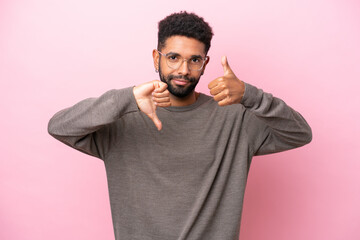 Young Brazilian man isolated on pink background making good-bad sign. Undecided between yes or not