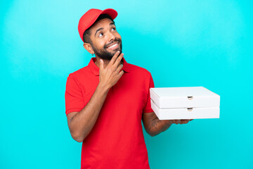 Pizza delivery Brazilian man with work uniform picking up pizza boxes isolated on blue background...