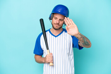Baseball player with helmet and bat isolated on blue background making stop gesture and disappointed
