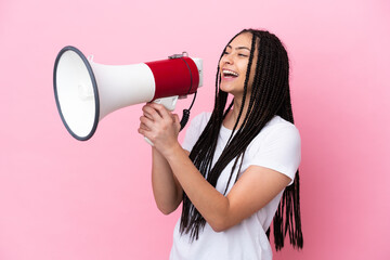 Teenager girl with braids over isolated pink background shouting through a megaphone to announce...