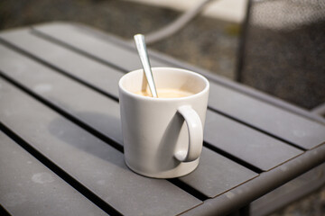 A glass of warm coffee with milk in a white ceramic cup on a gray iron table with a blurred background