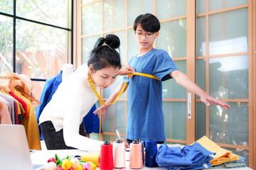 Asian women fashion designer  working and measure the customer in the showroom,  Lifestyle Stylish tailor clothing design and cutting cloths in studio.  Business small Concept.