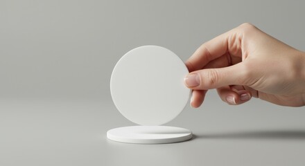 Hand Holding a White Circular Coaster on Gray Background