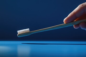 Fototapeta premium A hand delicately holds a bamboo toothbrush against a deep blue backdrop, showcasing eco-friendly oral hygiene.