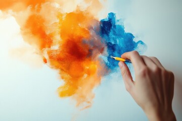A hand delicately blends orange and blue hues on a canvas, creating an abstract artwork.