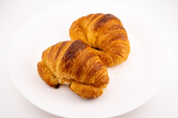 Two golden-brown croissants are positioned on a stark white surface.
