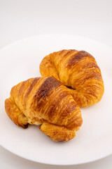Two golden-brown croissants are positioned on a stark white surface.