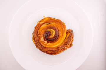 A single, golden-brown cinnamon roll, also known as a pain aux raisins or escargot pastry, is...