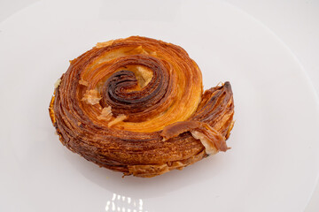 A single, golden-brown cinnamon roll, also known as a pain aux raisins or escargot pastry, is...
