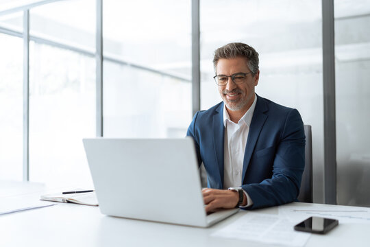 Mature Indian or Latin hispanic business man ceo manager using laptop computer typing in modern office. Middle eastern smiling senior businessman entrepreneur sitting at desk working on pc. Copy space