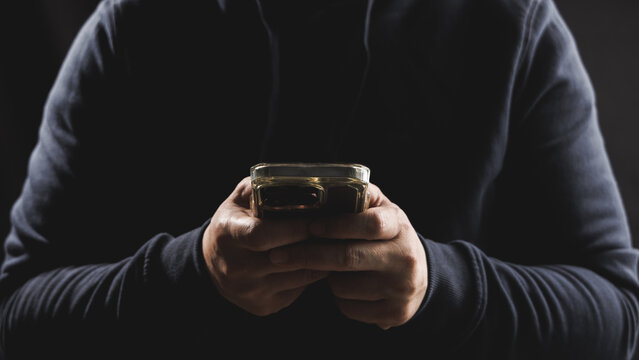 Man hand using smartphone in dark and moody tone. Concept of cybersecurity technology.