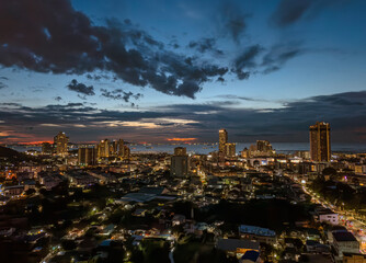 Evening skyline of a bustling coastal city with ships on the horizon during sunset